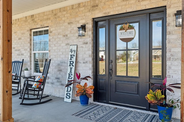 entrance to property featuring a porch and brick siding