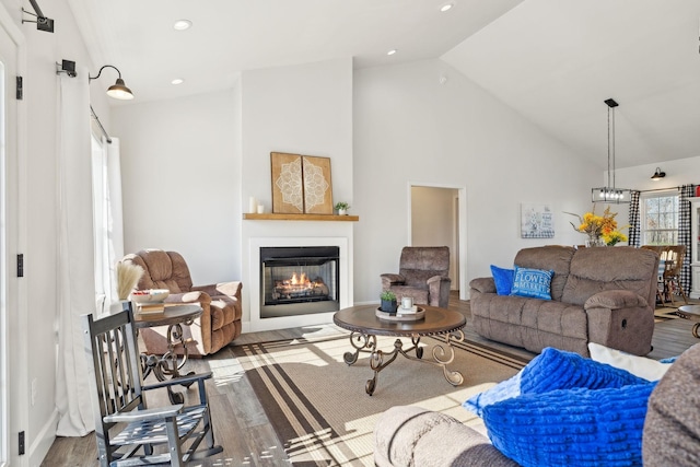 living area featuring high vaulted ceiling, wood finished floors, a glass covered fireplace, and recessed lighting