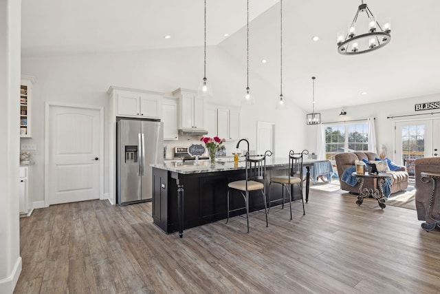 kitchen featuring stainless steel fridge, a center island with sink, a breakfast bar, wood finished floors, and white cabinetry