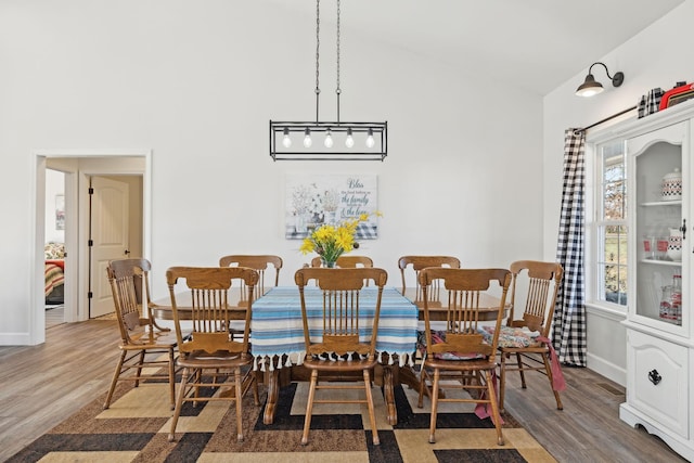 dining space with high vaulted ceiling, baseboards, and wood finished floors