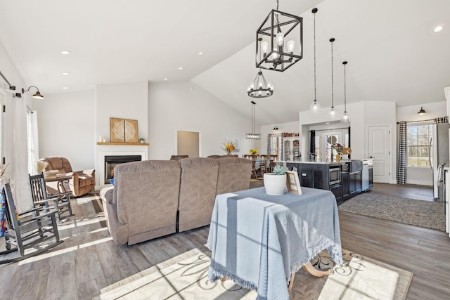 living room featuring a warm lit fireplace, recessed lighting, wood finished floors, vaulted ceiling, and an inviting chandelier