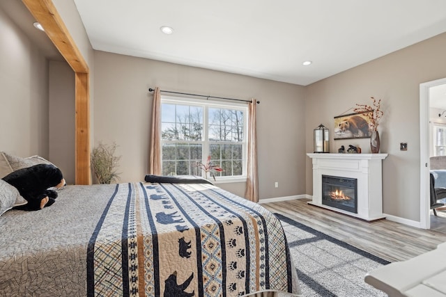 bedroom featuring recessed lighting, baseboards, wood finished floors, and a glass covered fireplace