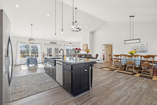 kitchen featuring light stone counters, french doors, stainless steel appliances, dark cabinets, and light wood-type flooring