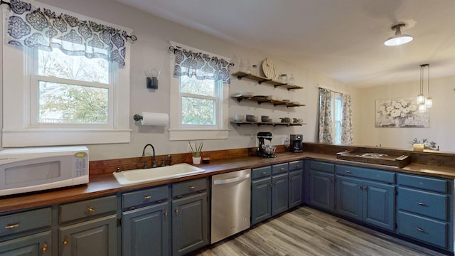 kitchen with light wood finished floors, white microwave, stainless steel dishwasher, blue cabinetry, and a sink