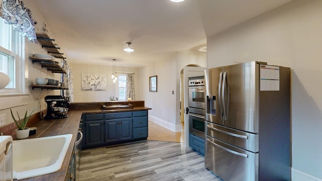 kitchen featuring light wood-style flooring, appliances with stainless steel finishes, blue cabinets, a peninsula, and open shelves