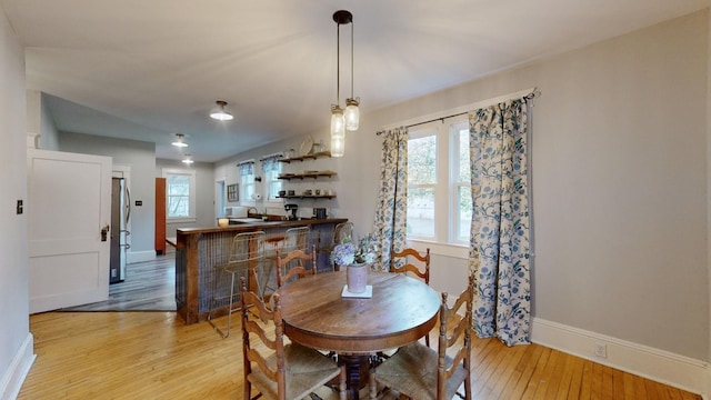 dining area with bar, light wood-style flooring, and baseboards