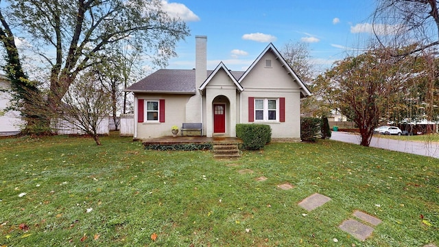 tudor home with brick siding, fence, roof with shingles, a chimney, and a front yard