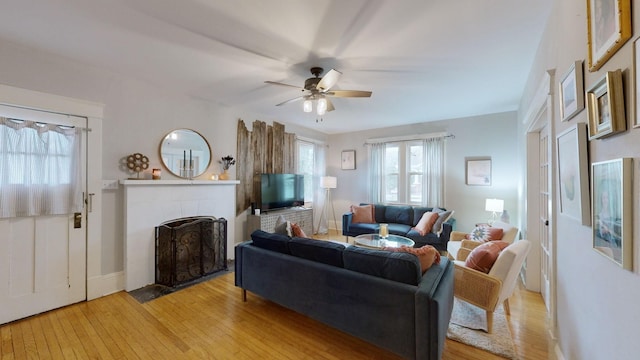 living area with baseboards, a tiled fireplace, light wood-style flooring, and a ceiling fan