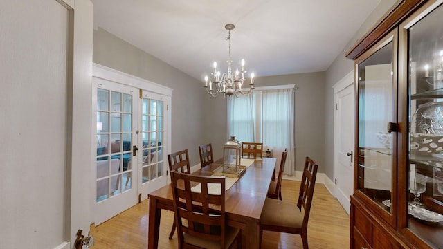 dining space with baseboards, french doors, light wood-type flooring, and an inviting chandelier