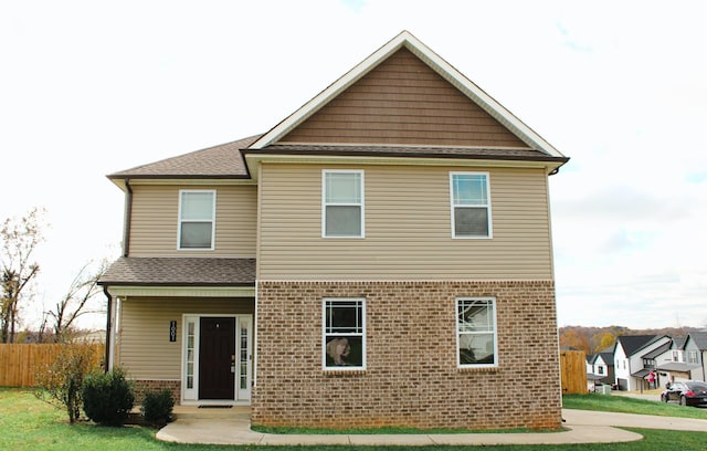 back of property with brick siding, a shingled roof, fence, and a yard