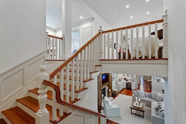 stairway with recessed lighting, a wainscoted wall, a decorative wall, wood finished floors, and ornamental molding