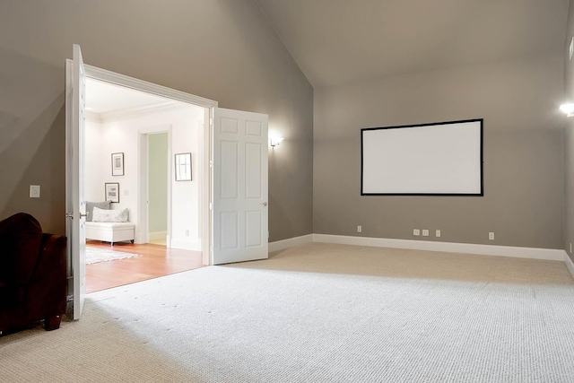 cinema room featuring high vaulted ceiling, light colored carpet, and baseboards