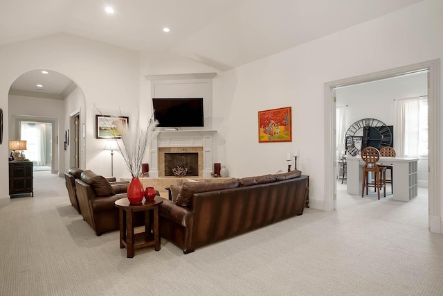 living room featuring lofted ceiling, a fireplace, arched walkways, and light colored carpet