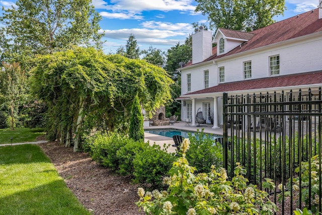 exterior space featuring an outdoor pool, a lawn, a patio, a chimney, and fence