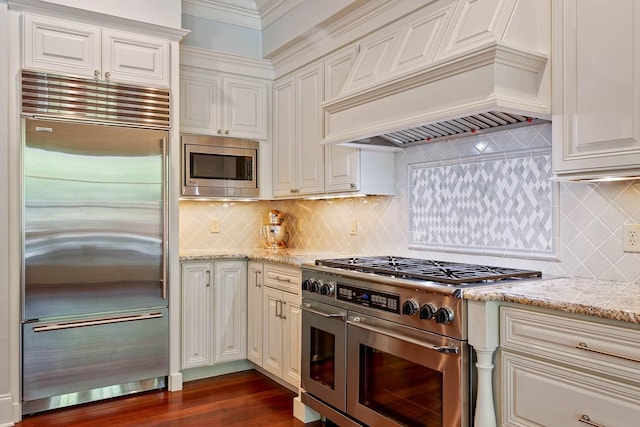 kitchen with tasteful backsplash, dark wood-style floors, custom range hood, built in appliances, and light stone countertops