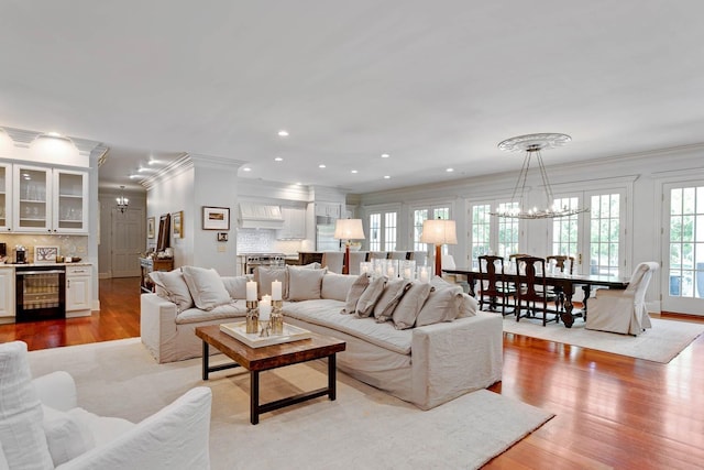 living area featuring recessed lighting, light wood-style floors, ornamental molding, a chandelier, and beverage cooler