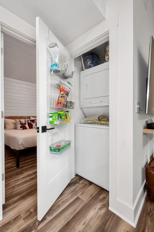 washroom featuring laundry area, stacked washer / drying machine, and wood finished floors