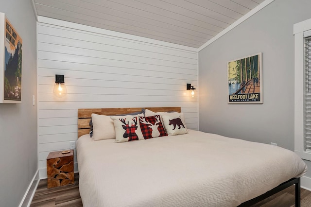 bedroom featuring wooden walls, baseboards, lofted ceiling, ornamental molding, and wood finished floors