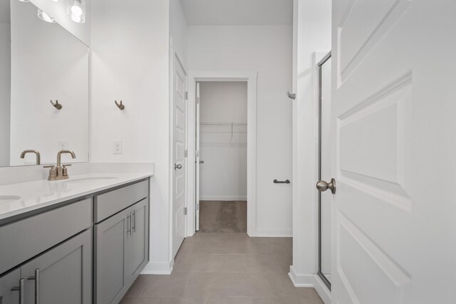 full bathroom with tile patterned flooring, a sink, double vanity, a stall shower, and a walk in closet