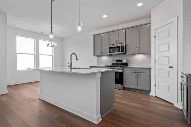 kitchen featuring appliances with stainless steel finishes, a sink, a kitchen island with sink, and gray cabinetry