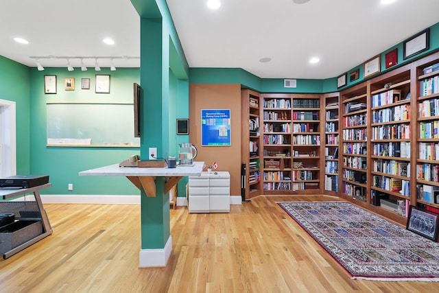 office area with wood finished floors, visible vents, baseboards, wall of books, and rail lighting