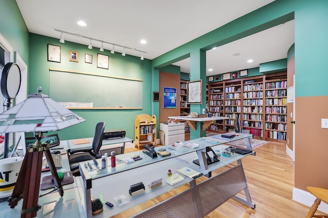 office space with wall of books, rail lighting, and wood finished floors