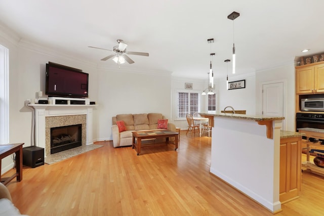 kitchen with light wood-style floors, a kitchen breakfast bar, black oven, ornamental molding, and stainless steel microwave