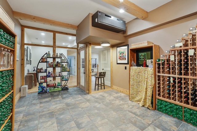 wine room featuring beam ceiling, stone finish floor, and baseboards