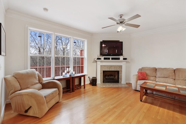 living area featuring light wood-type flooring, ceiling fan, a fireplace, and ornamental molding