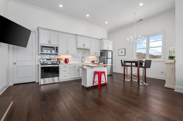 kitchen featuring a breakfast bar area, stainless steel appliances, light countertops, backsplash, and crown molding