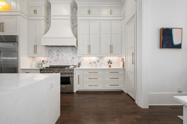 kitchen with premium appliances, premium range hood, white cabinets, backsplash, and dark wood finished floors