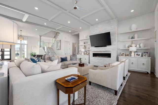 living room with stairs, a stone fireplace, built in shelves, and dark wood-style flooring