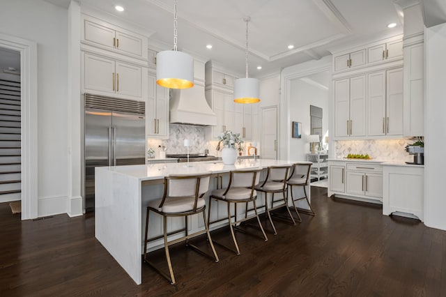 kitchen featuring light countertops, backsplash, stainless steel built in fridge, dark wood-style floors, and custom range hood