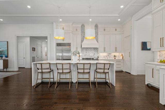 kitchen featuring dark wood-style flooring, tasteful backsplash, light countertops, custom range hood, and stainless steel built in fridge