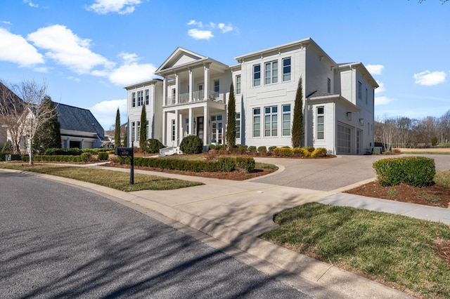 neoclassical home featuring a balcony, driveway, an attached garage, and stucco siding