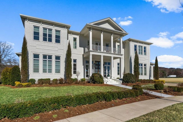 greek revival inspired property featuring a balcony, brick siding, a front lawn, and french doors