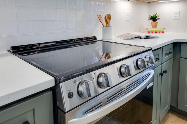 details with green cabinets, light countertops, backsplash, and stainless steel range with electric cooktop