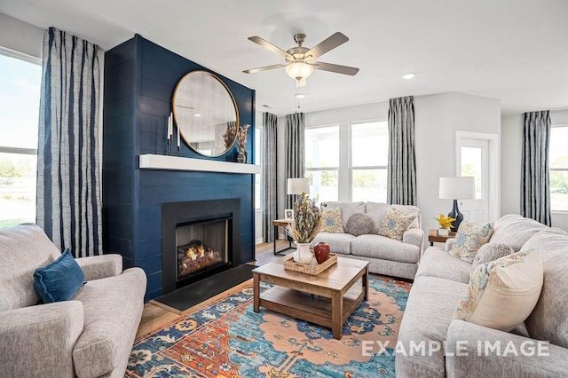 living room with a large fireplace, a ceiling fan, and wood finished floors