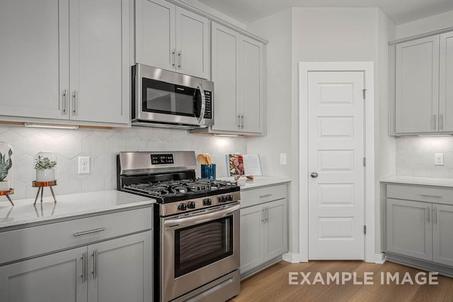 kitchen featuring stainless steel appliances, light countertops, decorative backsplash, gray cabinetry, and light wood-style floors