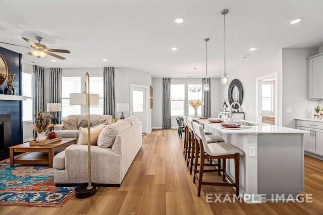 kitchen with light wood finished floors, a fireplace, a sink, and a center island with sink