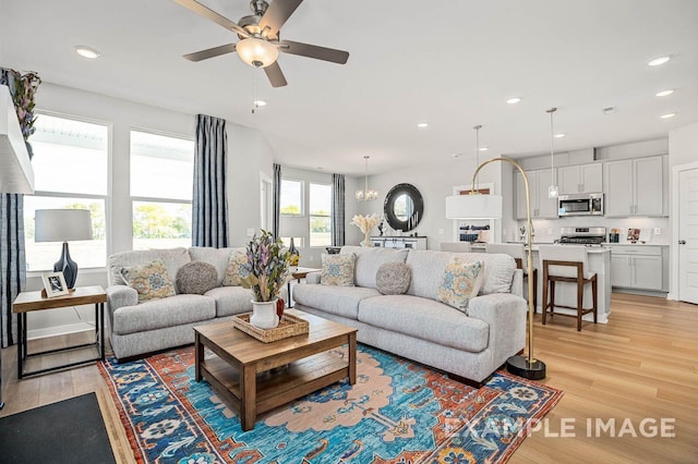 living room with ceiling fan with notable chandelier, light wood-type flooring, and recessed lighting