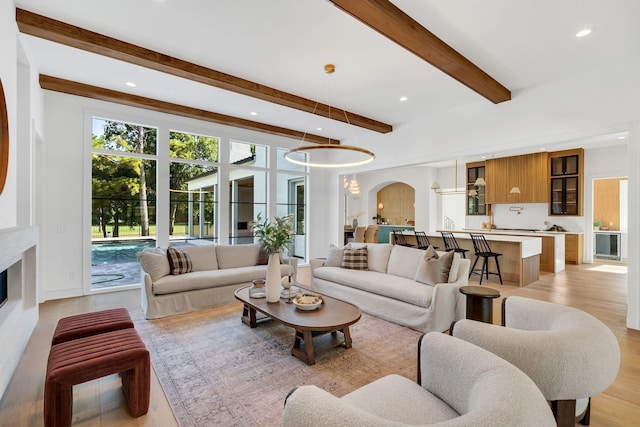 living room featuring arched walkways, light wood-style floors, beam ceiling, and recessed lighting