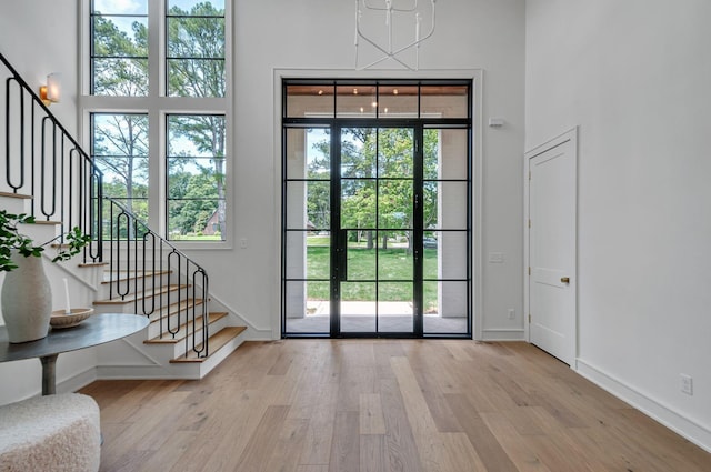 doorway to outside featuring light wood-style floors, baseboards, stairway, and a high ceiling