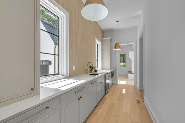 kitchen featuring light wood-style flooring, a sink, baseboards, light countertops, and pendant lighting