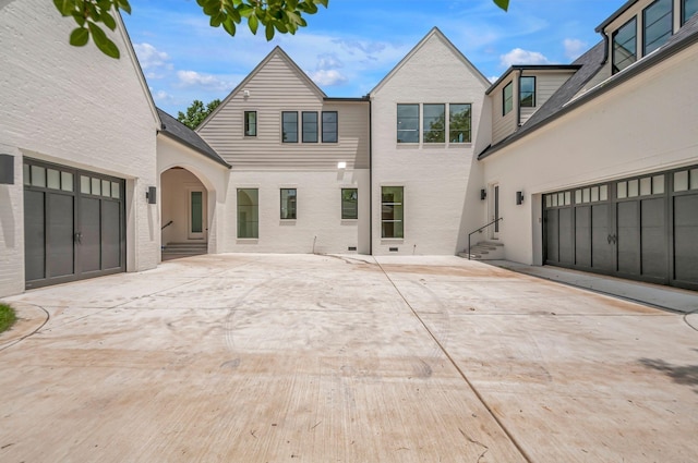 rear view of house with entry steps, driveway, brick siding, and a patio area