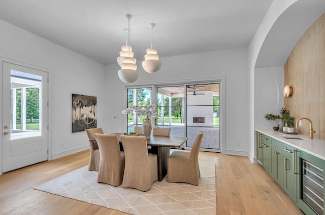 dining space featuring light wood-style floors, wine cooler, a chandelier, and baseboards