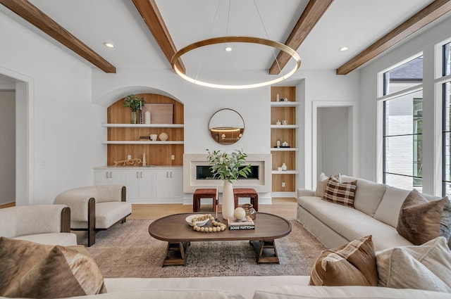 living room with built in shelves, beamed ceiling, and wood finished floors