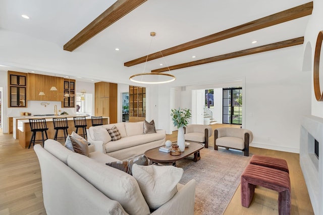 living area featuring recessed lighting, a fireplace, baseboards, light wood-style floors, and beam ceiling