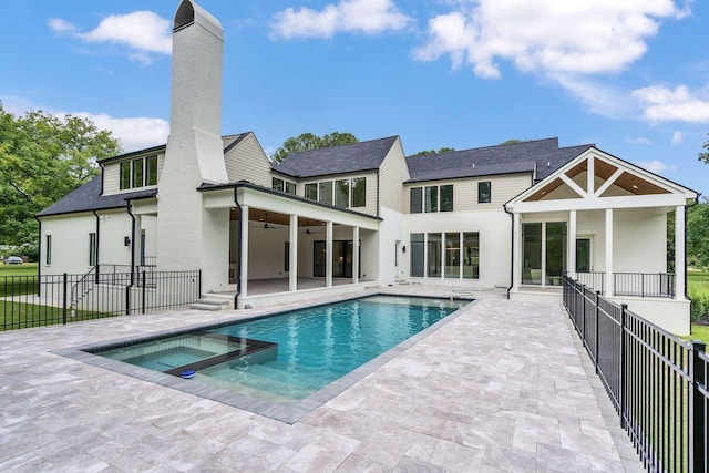 rear view of property with a ceiling fan, a patio, a chimney, fence, and a pool with connected hot tub