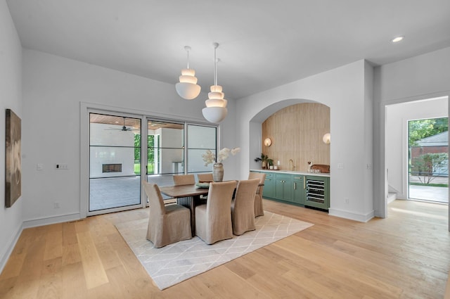 dining room featuring light wood-style flooring, recessed lighting, beverage cooler, bar area, and baseboards